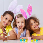 three children in bright clothes eating Easter eggs