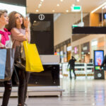 Two best friends collegue girls posing at modern shopping mall background